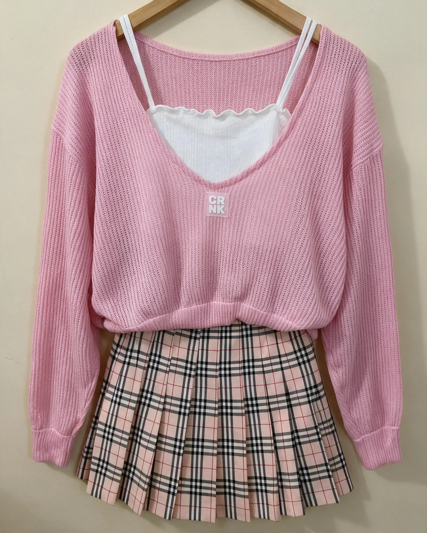 Flat-lay pink knit cardigan and plaid skirt styled on a wooden hanger